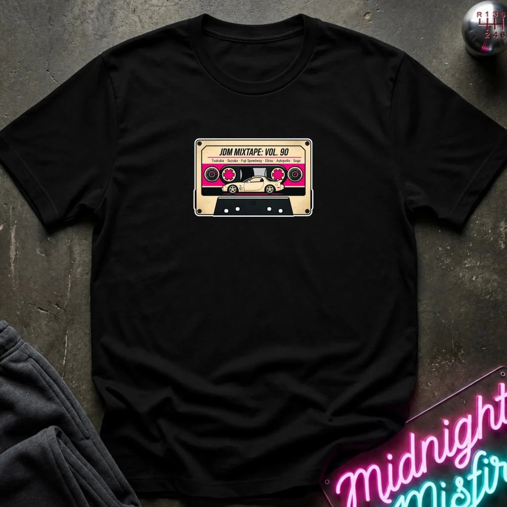 A black crewneck t-shirt laid flat on a dark textured surface, featuring a retro cassette tape graphic on the chest with the text 'JDM MIXTAPE VOL.
