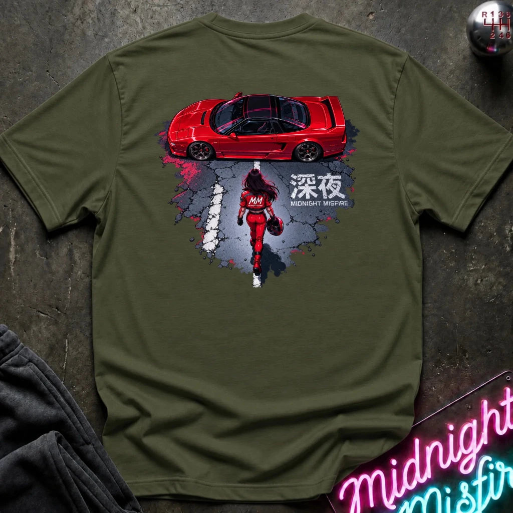 An olive green short-sleeve graphic T-shirt laid flat on a dark textured surface. The shirt features a large back print showing a red sports car above a red racer in a splattered gray and black design