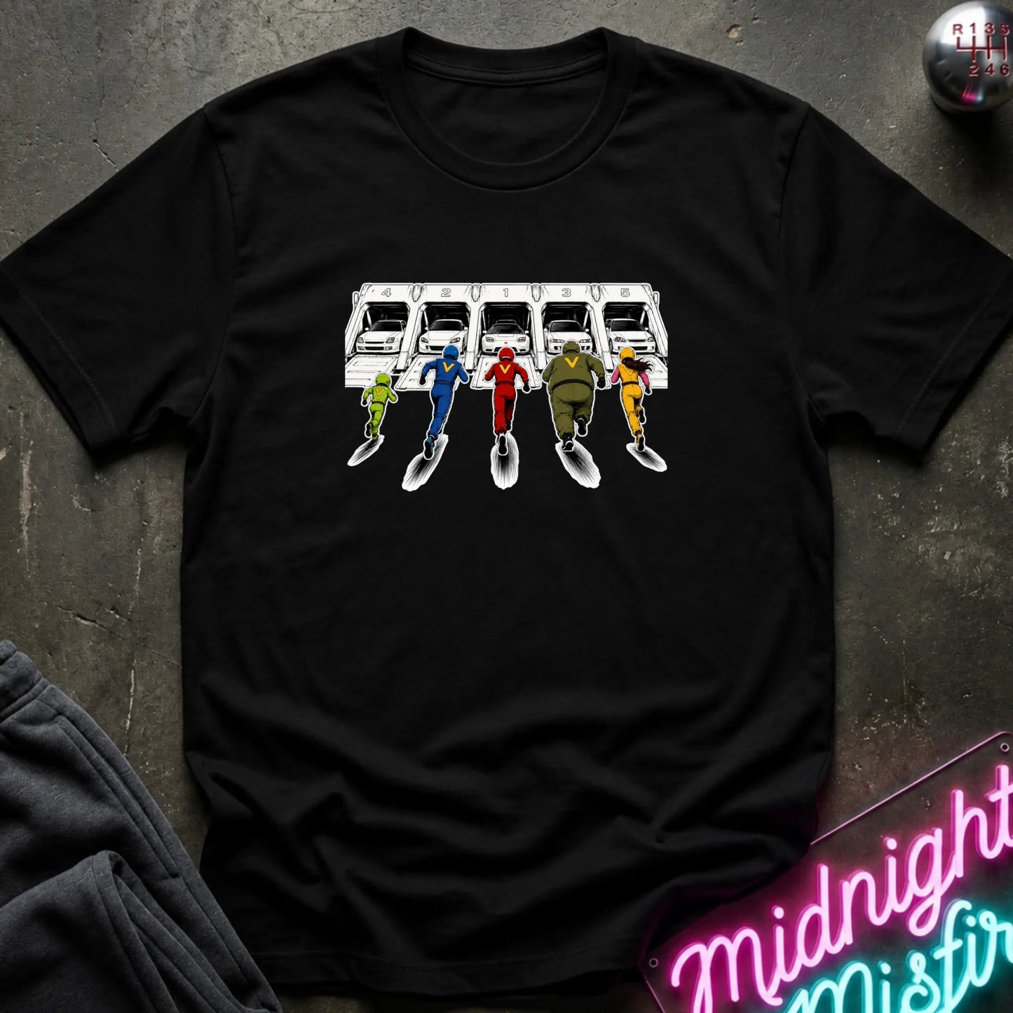 A black short-sleeve graphic T-shirt laid flat on a dark textured surface. The shirt features a printed illustration of a white sports cars in 5 different launch  pods.