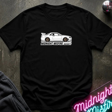 black short-sleeve t-shirt laid flat on a dark textured surface, featuring a white sports car graphic and the text 'MIDNIGHT MISFIRE '