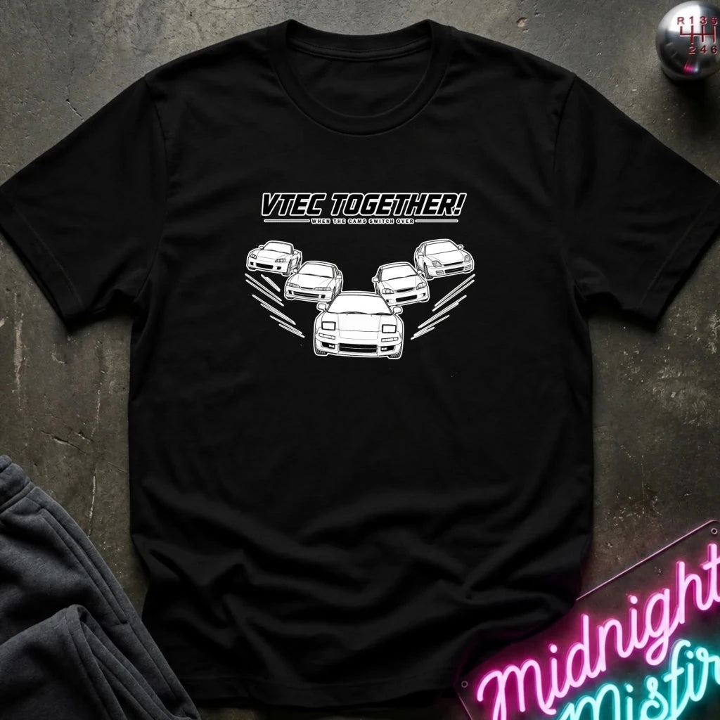 A black short-sleeve graphic t-shirt laid flat on a dark textured surface. The shirt features a white graphic of several cars with the text 'VTECs TOGETHER!' 