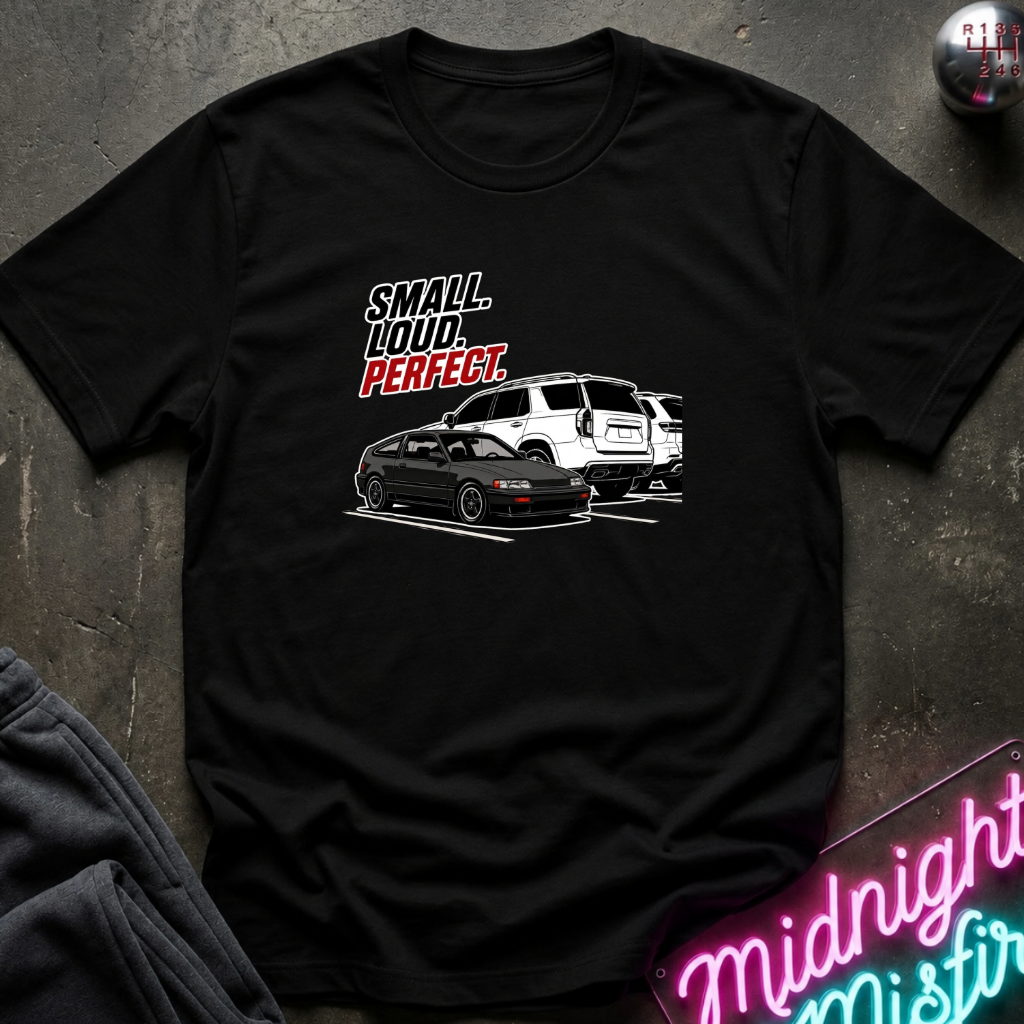 A black short-sleeve graphic t-shirt laid flat on a dark textured surface. The graphic features the texts.