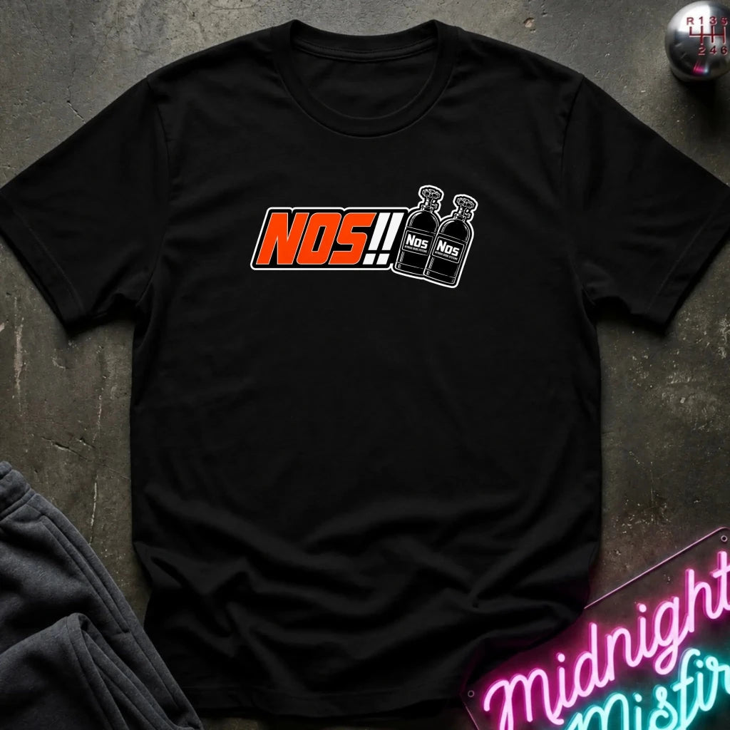 A black short-sleeve t-shirt laid flat on a dark textured surface, featuring a graphic print with the word 'NOS!!' in orange and white, alongside two illustrated bottles labeled 'NOS'. 