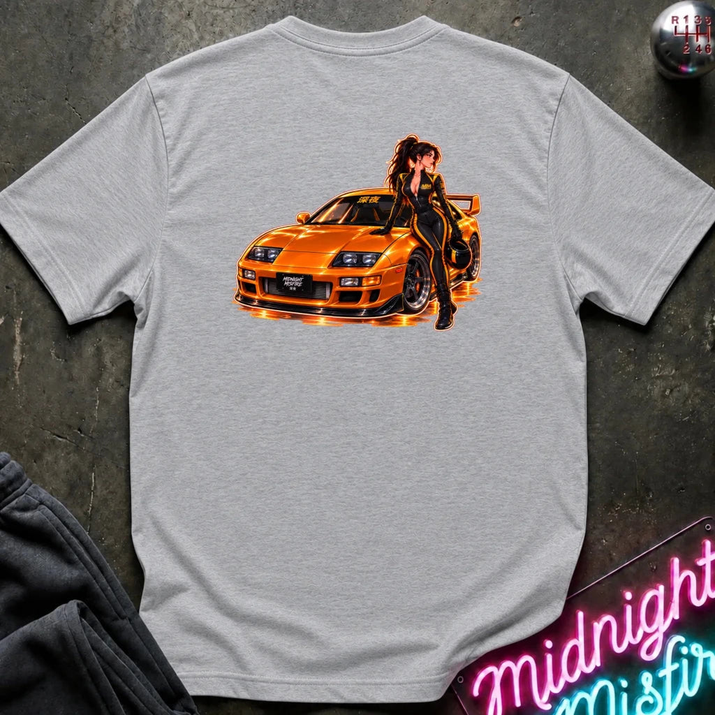 A light gray heather crewneck t-shirt featuring a graphic print of a woman in a black jumpsuit posing on an orange sports car, displayed flat on a dark textured background.