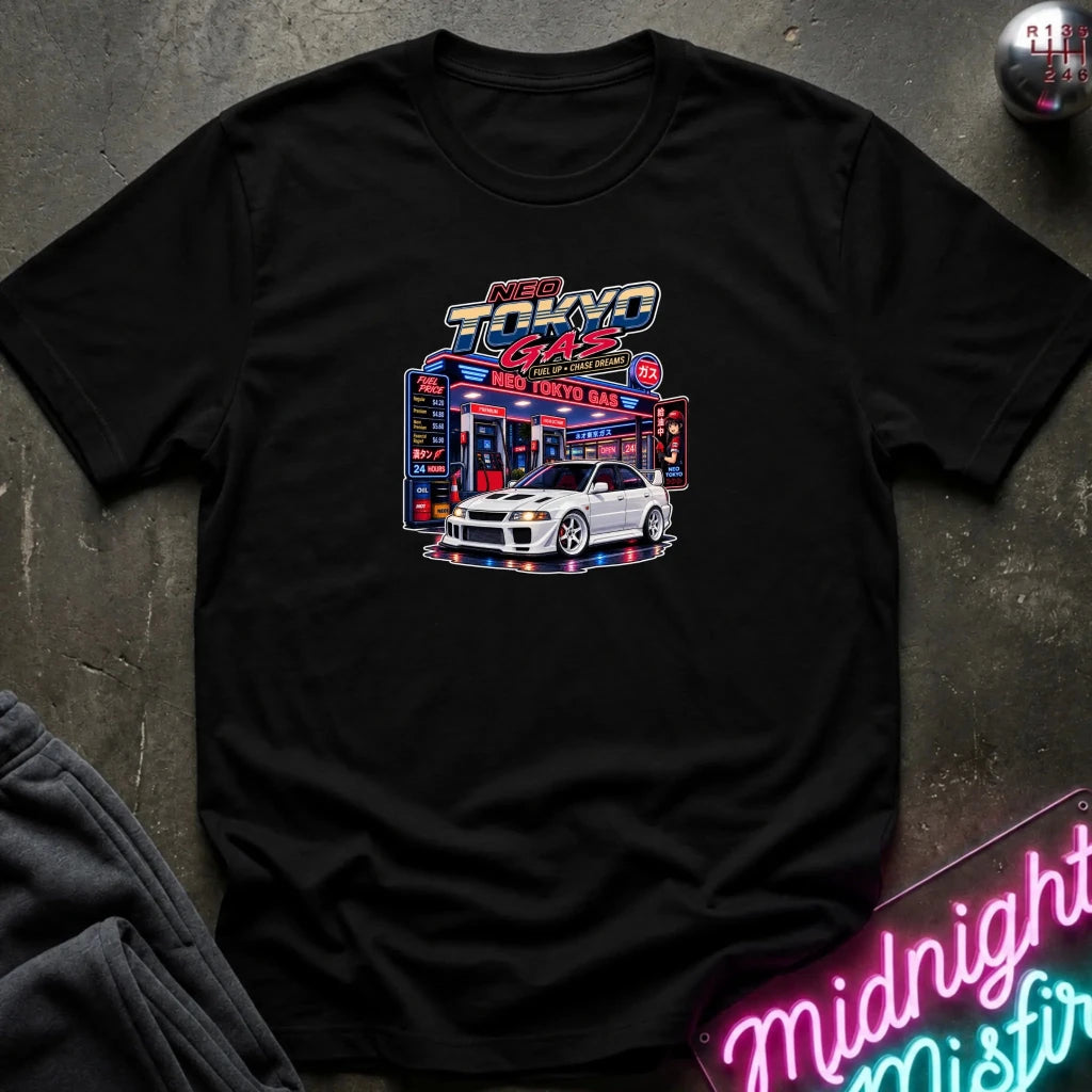 A black short-sleeve crewneck t-shirt featuring a 'Neo Tokyo Gas' graphic with a white sports car, laid flat on a dark textured surface with a neon sign and sweatpants as props.