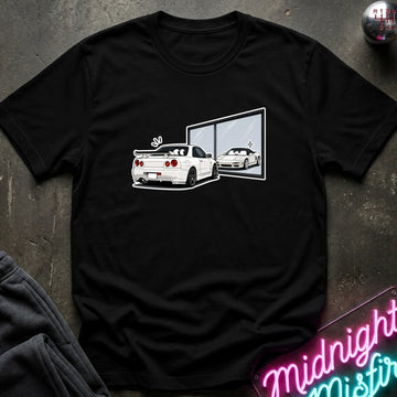 A black short-sleeve t-shirt laid flat on a dark textured surface, featuring a graphic print of a white sports car and its reflection in a window. A neon sign is partially visible in the bottom right corner.