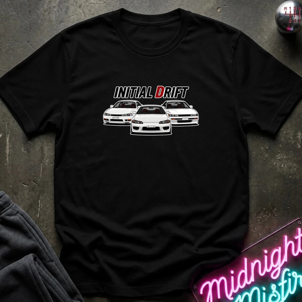 A black short-sleeve graphic t-shirt laid flat on a dark textured surface. The shirt features a white and red graphic print that reads 'INITIAL DRIFT' above three white drift cars.
