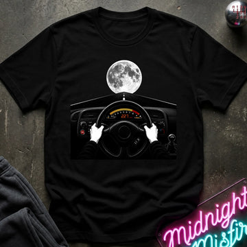 black crewneck t-shirt laid flat on a dark textured surface, featuring a graphic print of a driver's hands on a steering wheel with a full moon above the dashboard. 