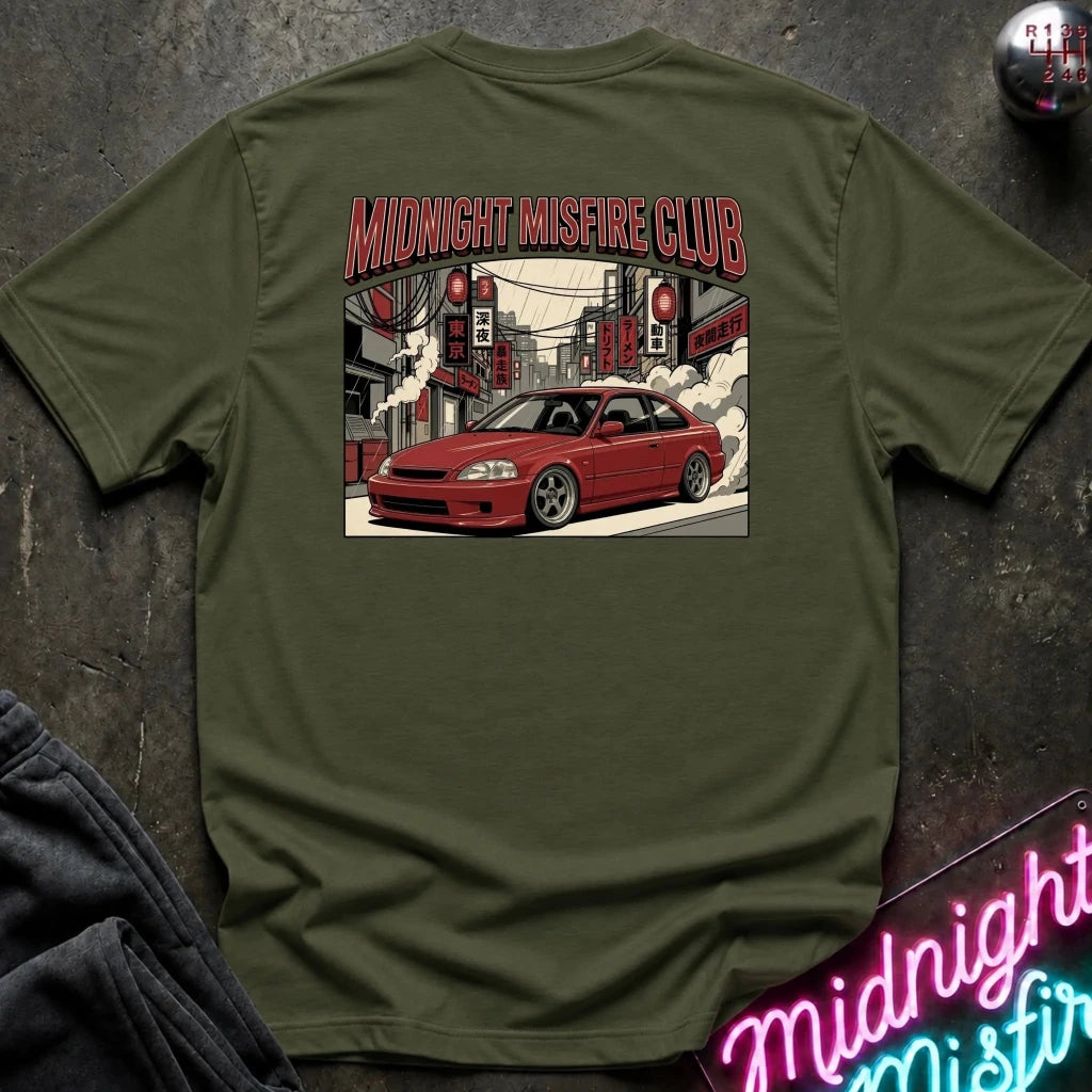 An olive green crewneck t-shirt laid flat on a dark textured surface, featuring a large graphic print on the back with the text 'MIDNIGHT MISFIRE CLUB' and an illustration of a red sports car in a city street.