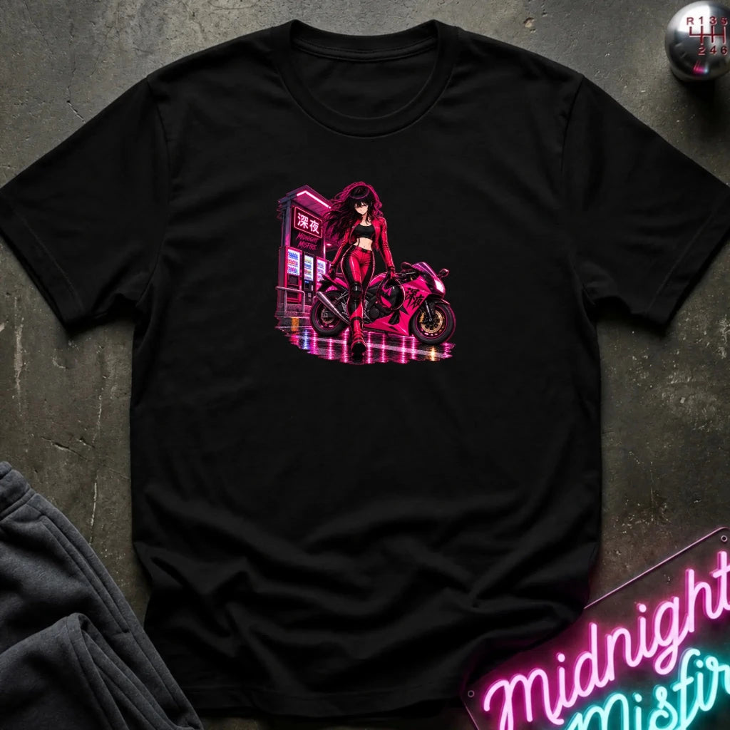 A black short-sleeve t-shirt laid flat on a dark textured surface, featuring a colorful graphic print of an anime-style woman in a red outfit standing next to a pink motorcycle with neon signs. 