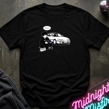 A black short-sleeve graphic t-shirt laid flat on a dark textured surface. The graphic shows a white line-art drawing of a person with a car and a speech bubble 
