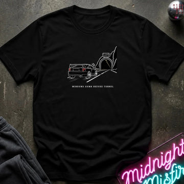 A black short-sleeve t-shirt laid flat on a dark textured surface, featuring a black graphic of a classic car in a tunnel with the text.