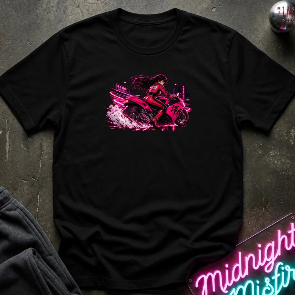 A black short-sleeve crewneck t-shirt laid flat on a dark textured surface, featuring a vibrant pink and red graphic of a woman riding a motorcycle with neon city lights and spray details. 