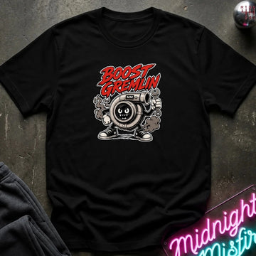 A black short-sleeve graphic T-shirt laid flat on a dark textured surface. The shirt features a cartoon character with a mustache and goggles, with the words 'BOOST GREMLIN' in red and white above it.