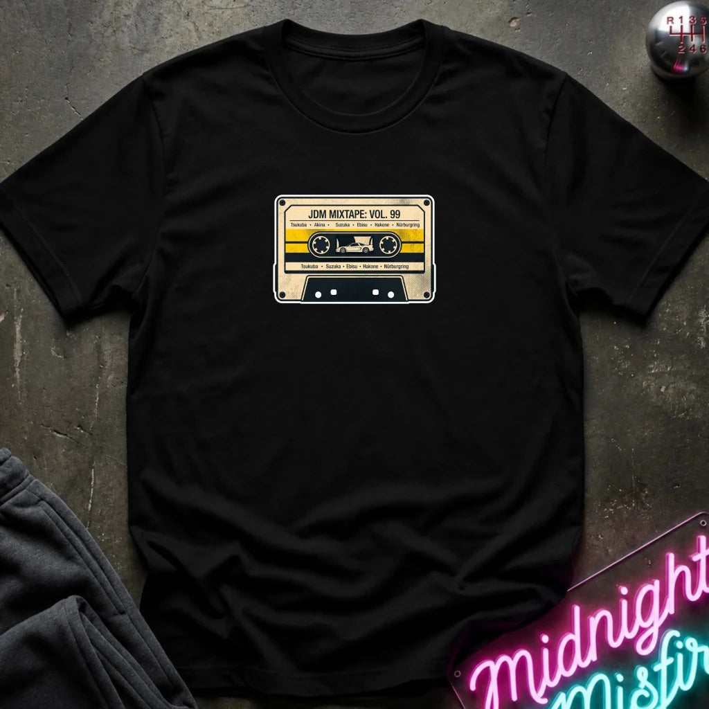 black crewneck t-shirt laid flat on a dark textured surface, featuring a retro cassette tape graphic on the chest with the text 'JDM MIXTAPE VOL.