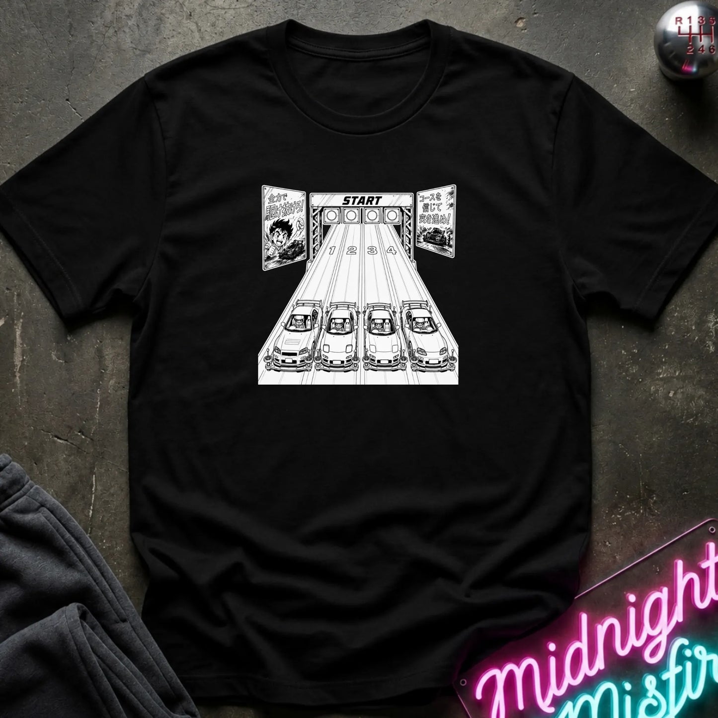 A black short-sleeve t-shirt laid flat on a dark textured surface, featuring a black-and-white graphic of 4 cars lined up at a racing on a track.