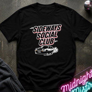 A black short-sleeve graphic t-shirt laid flat on a dark textured surface. The shirt features a white and red graphic print that reads 'SIDEWAYS SOCIAL CLUB' above a white car illustration.