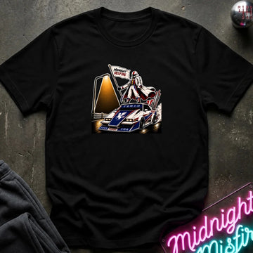 A black short-sleeve crewneck t-shirt featuring a graphic print of a vintage race car with a driver and a large screen, styled flat on a dark textured surface with a neon sign and sweatpants partially visible.