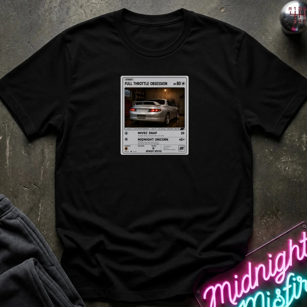 black crewneck t-shirt laid flat on a dark textured surface. The shirt features a graphic print styled like a retro card