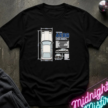 A black short-sleeve graphic t-shirt laid flat on a dark textured surface. The shirt features a white and blue graphic print of a classic car with technical-style diagrams and the text 'AE86' and 'JAPAN'.