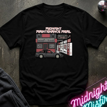 A black short-sleeve graphic t-shirt laid flat on a dark textured surface. The shirt features a retro-style illustration of a car parked outside a 'Midnight Maintenance Meal' shop, with pink and white text.