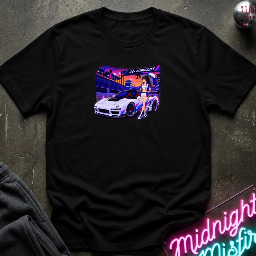 A black short-sleeve t-shirt laid flat on a dark textured surface, featuring a colorful graphic print of a white sports car and a woman in a neon-lit scene. 