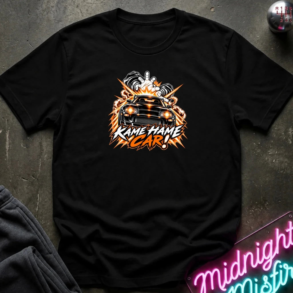 black short-sleeve graphic t-shirt laid flat on a dark textured surface. The shirt features a red, white, and black graphic of a car with the text 'KAME HAME CAR!' in stylized lettering.