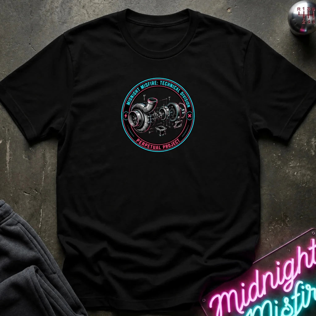A black short-sleeve t-shirt laid flat on a dark textured surface, featuring a circular chest graphic with a technical engine illustration and the words 