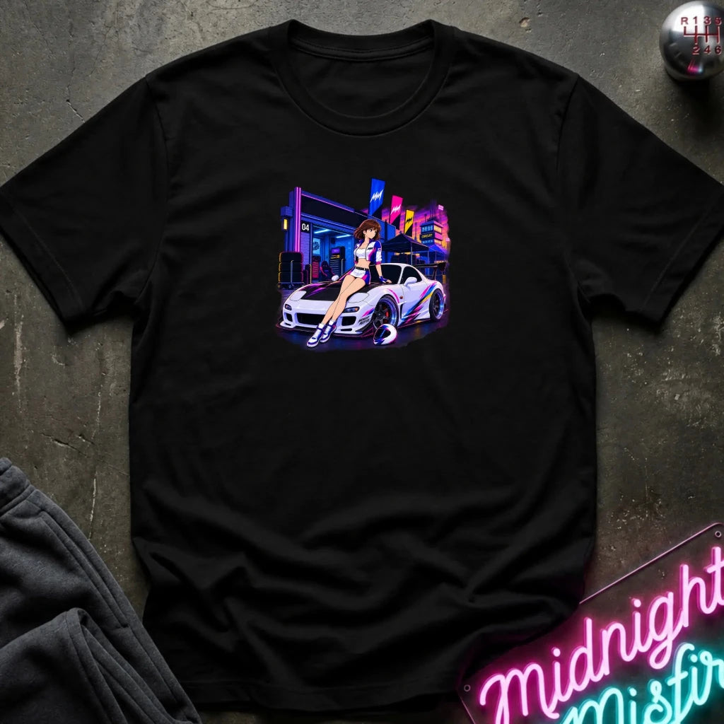 A black  short-sleeve t-shirt laid flat on a dark textured surface, featuring a colorful graphic print of a white sports car and a woman in a neon-lit scene. 