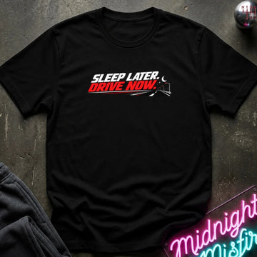 A black short-sleeve crewneck t-shirt laid flat on a dark textured surface. The shirt features a graphic print on the chest that reads 'SLEEP LATER.