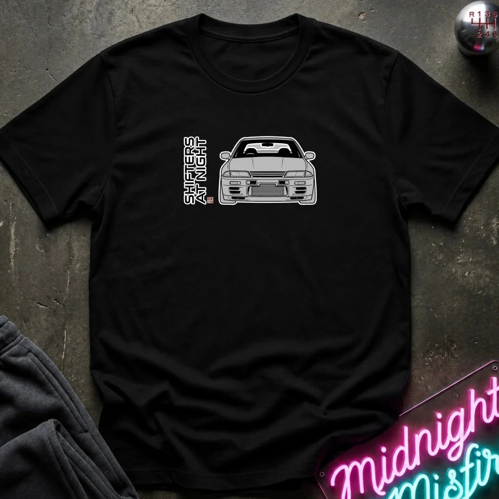 A black short-sleeve graphic t-shirt laid flat on a dark textured surface. The shirt features a white line-art graphic of a sports car and the vertical text
