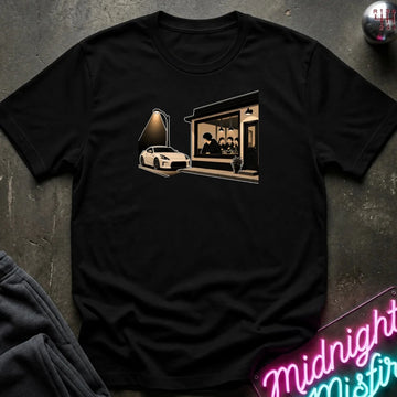 A black short-sleeve crewneck t-shirt laid flat on a dark textured surface, featuring a graphic print of a white sports car parked in front of a building with a glowing window. 