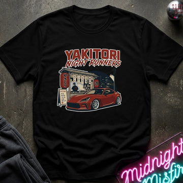 Black short-sleeve graphic t-shirt laid flat on a dark textured surface. The graphic features the text 'YAKITORI NIGHT RUNNERS'.