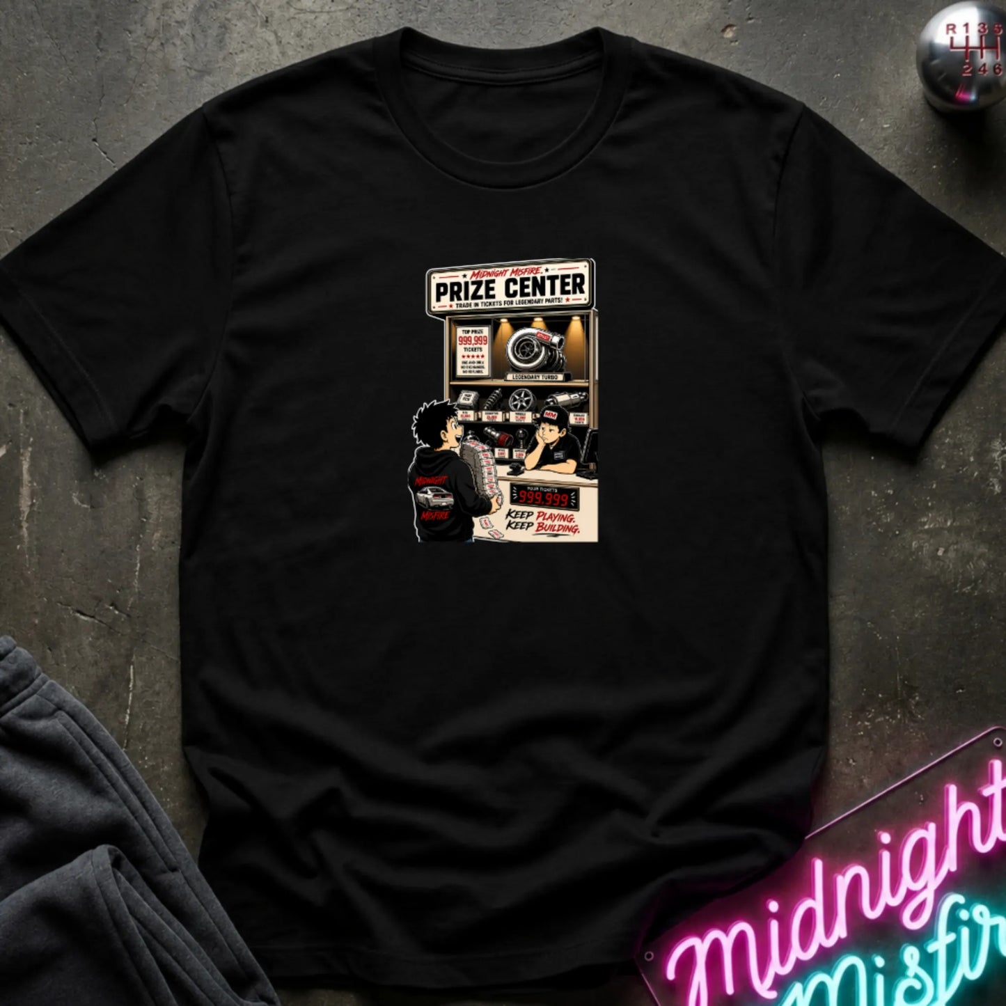 A black short-sleeve crewneck t-shirt laid flat on a dark textured surface, featuring a central graphic print of a prize center for car parts. 