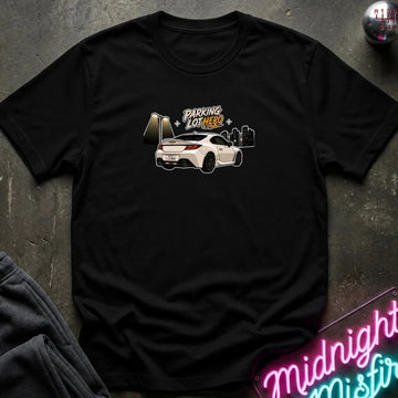 black crewneck t-shirt laid flat on a dark textured surface, featuring a graphic of a white sports car with the text 'PARKING LOT HERO'