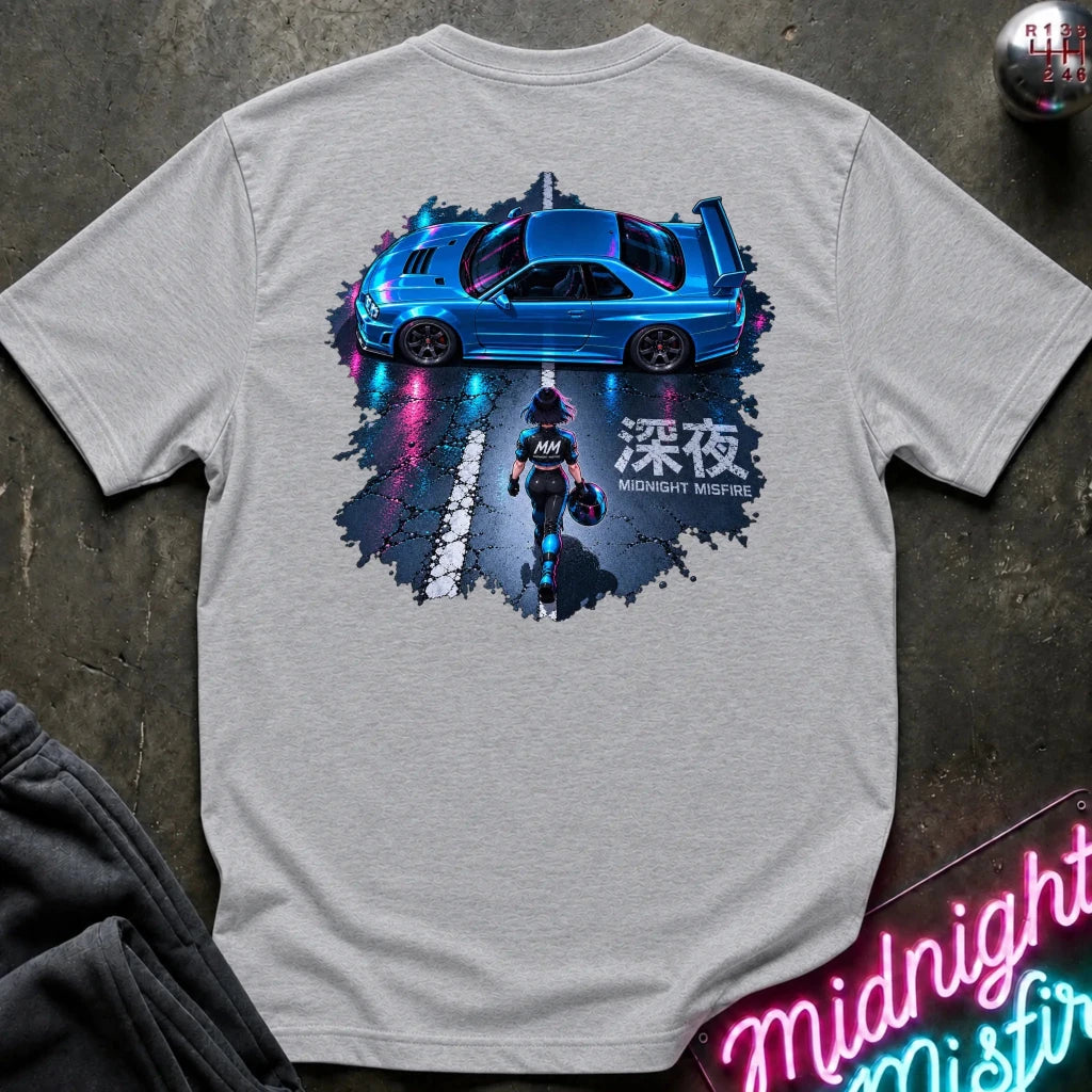 A light gray crewneck t-shirt featuring a large graphic print on the back of a blue sports car with a driver and Japanese text, styled flat on a dark textured surface.