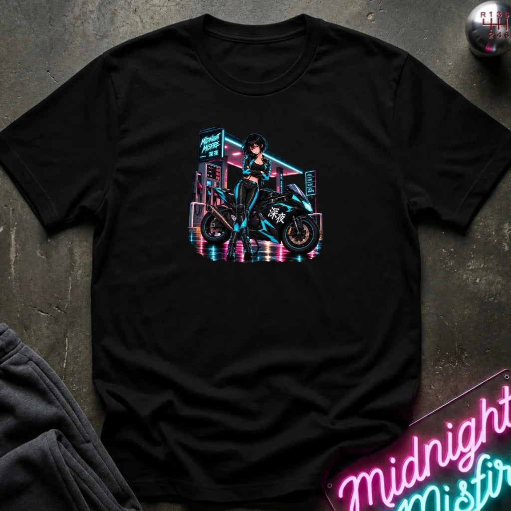 A black short-sleeve graphic t-shirt laid flat on a dark textured surface. The shirt features a colorful retro-futuristic graphic of a woman riding a motorcycle in front of a neon-lit building.