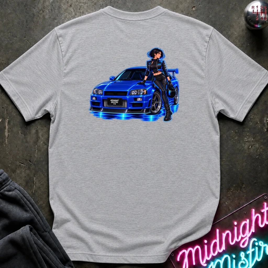 A light heather gray t-shirt laid flat on a dark textured surface, featuring a graphic print of a blue sports car with glowing blue lights and an anime-style woman standing beside it.