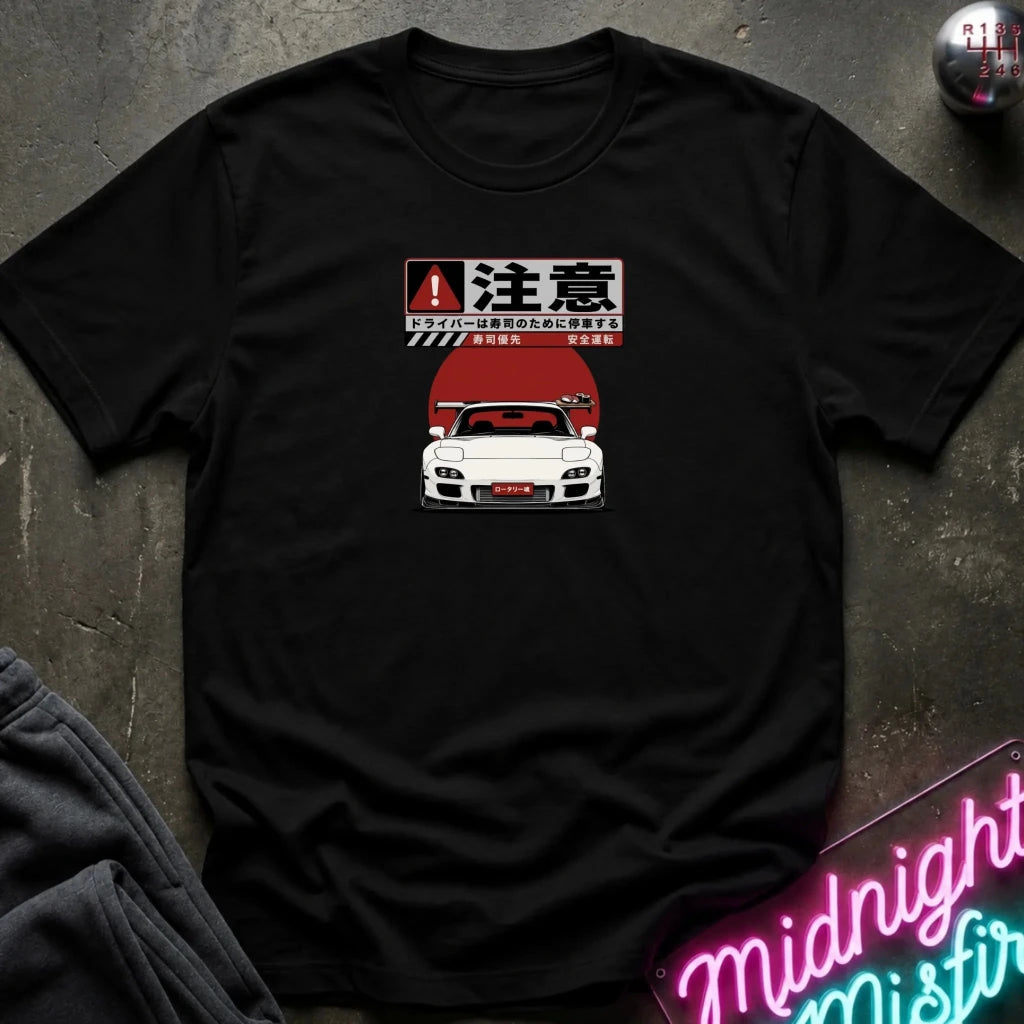 A black short-sleeve graphic t-shirt laid flat on a dark textured surface. The graphic features a white sports car with a red hood and Japanese text above it.