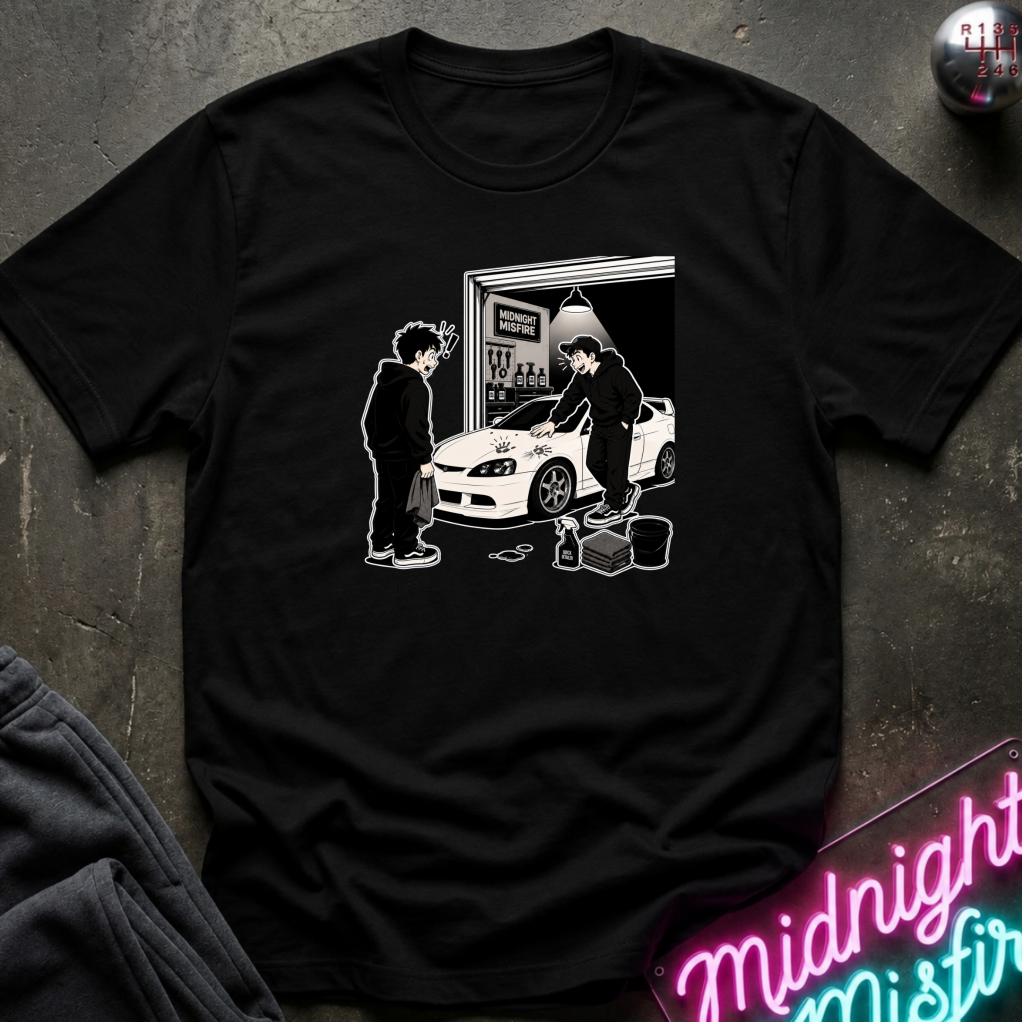 A black short-sleeve crewneck t-shirt laid flat on a dark textured surface, featuring a white graphic print of a person standing next to a white sports car in front of a garage door.