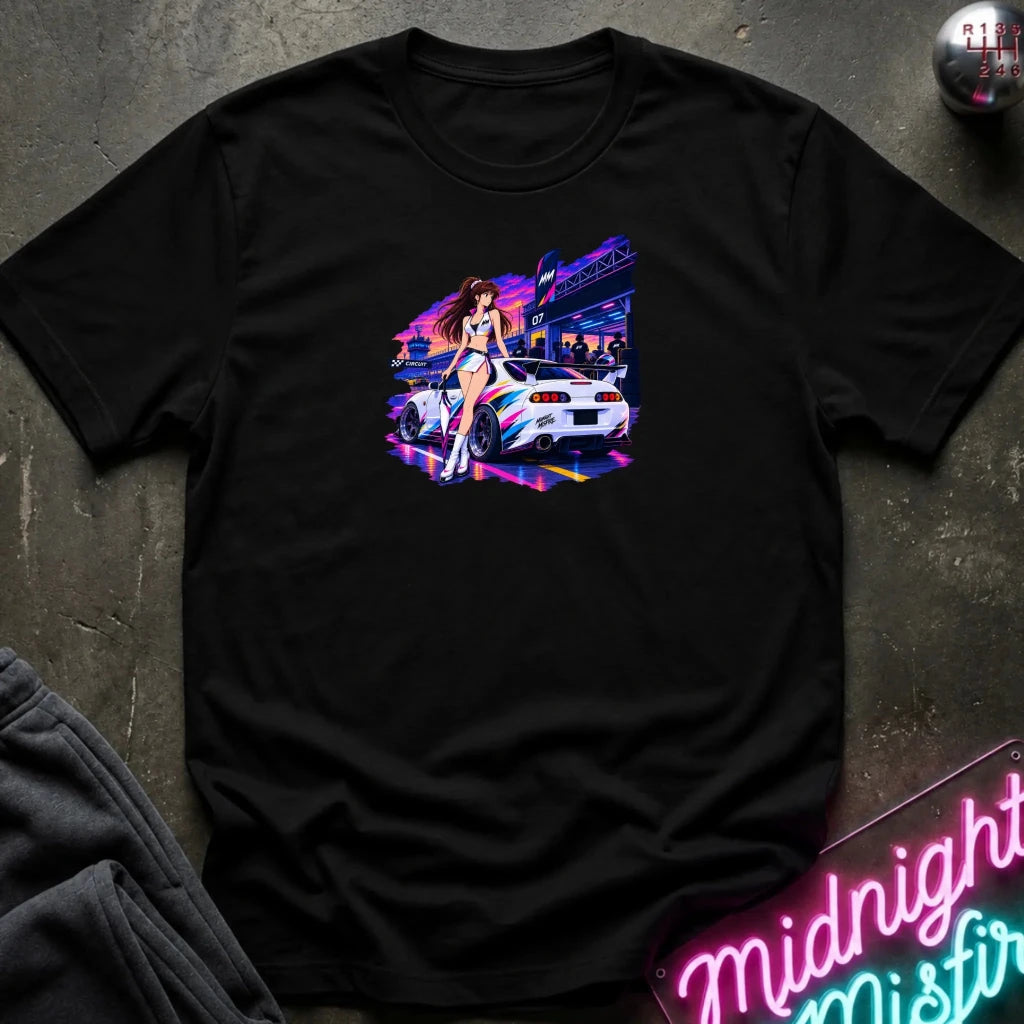 A black  short-sleeve t-shirt laid flat on a dark textured surface, featuring a colorful graphic print of a white sports car and a woman in a neon-lit scene. 