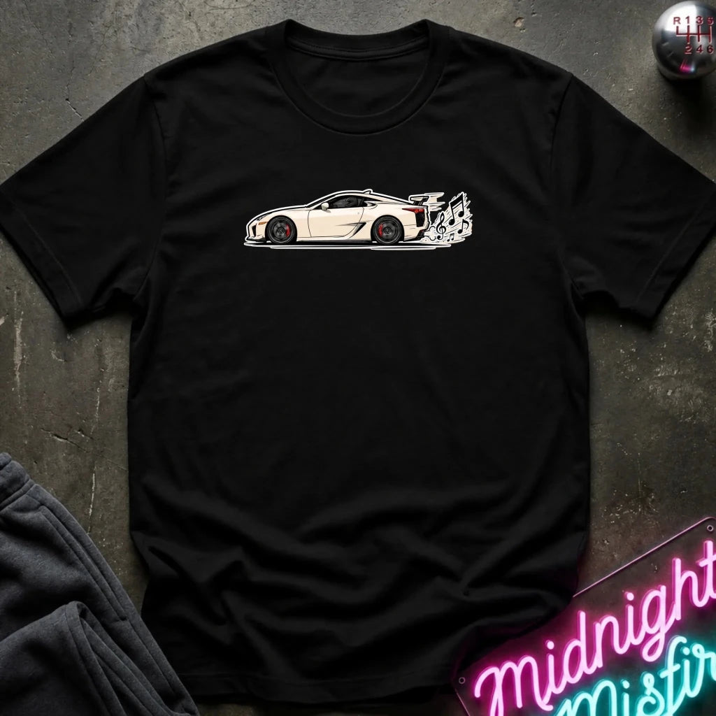 A black short-sleeve crewneck t-shirt featuring a white side-profile graphic of a sports car with a rear spoiler, laid flat on a dark textured surface with a neon sign and folded dark fabric visible at the edges.