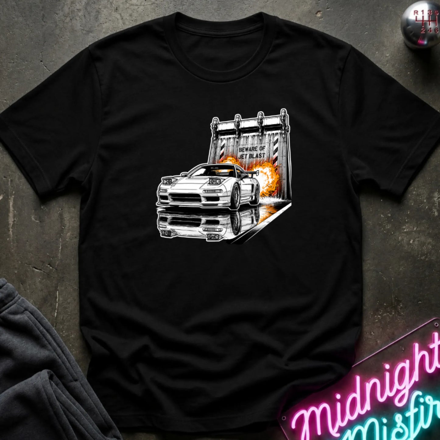 a black short-sleeve t-shirt laid flat on a dark textured surface, featuring a graphic print of a white sports car in front of a blast off area.