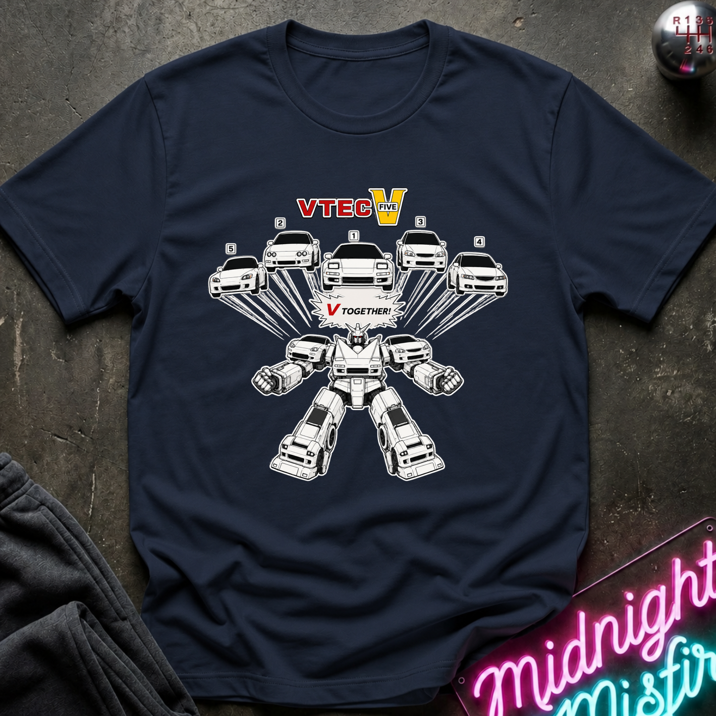 A navy blue graphic t-shirt laid flat on a dark textured surface. The shirt features a white line-art graphic of multiple cars arranged in a robot-like structure, with the text 'VTECH' in red and yellow and 'V TOGETHER' in red in the center.
