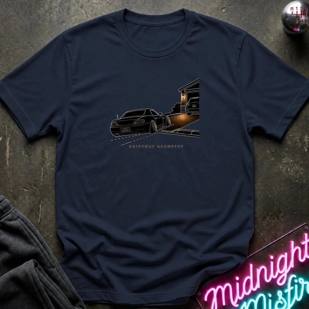 A navy blue short-sleeve t-shirt laid flat on a dark textured surface, featuring a graphic print of a black classic car going up the driveway.