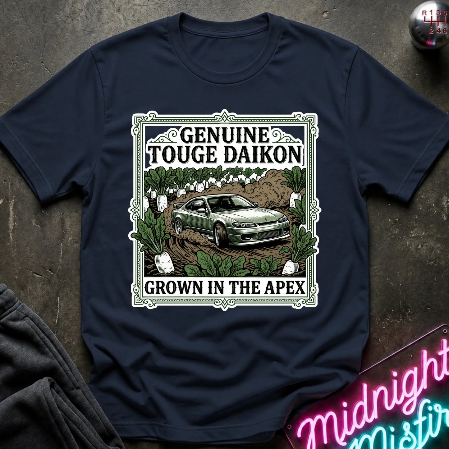 A navy blue short-sleeve graphic T-shirt laid flat on a dark textured surface. The shirt features a large rectangular front print with the words 'GENUINE TOUGHE DAIKON' and 'GROWN IN THE APEX'.