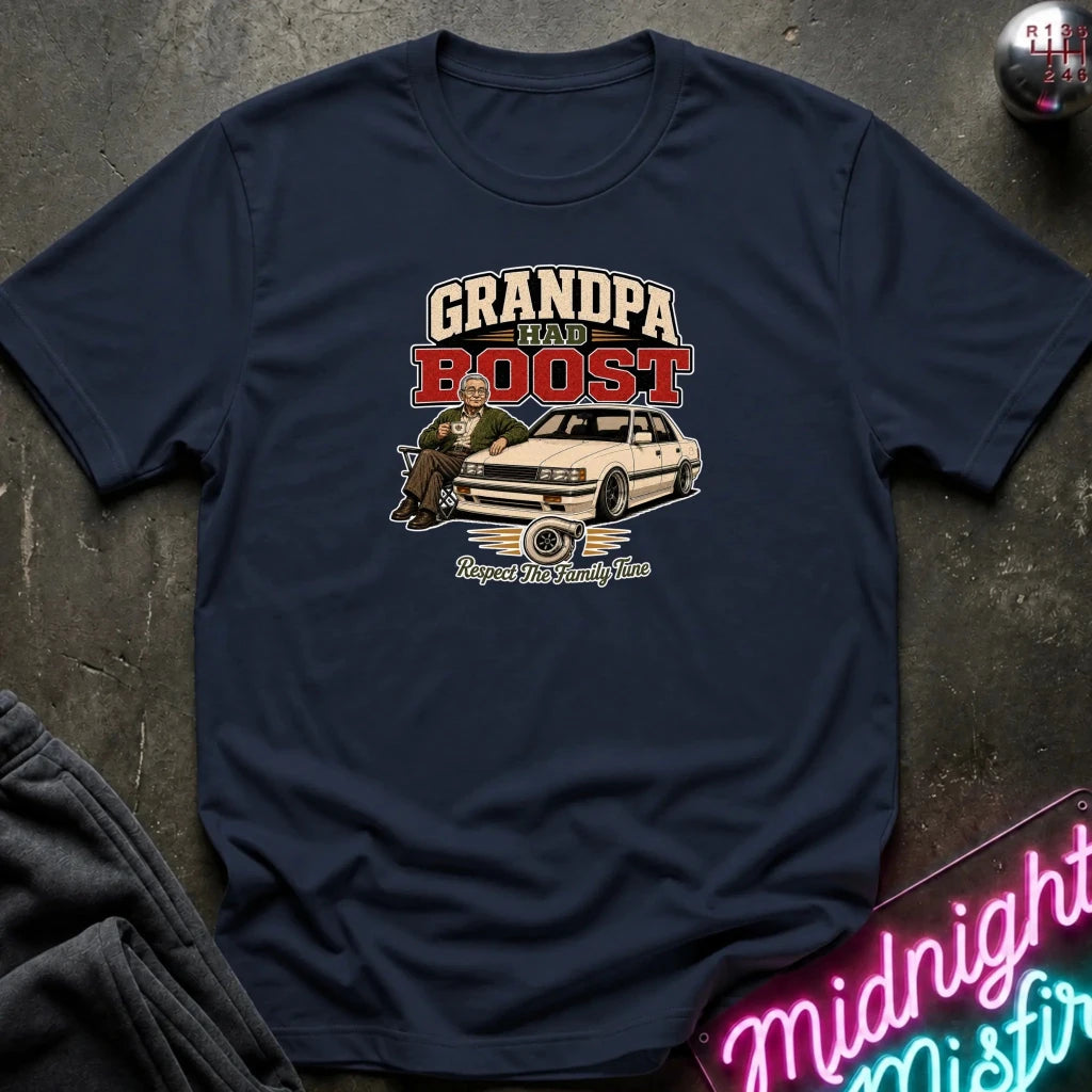 navy short-sleeve graphic t-shirt laid flat on a dark textured surface. The graphic features the text 'GRANDPA RAW BOOST' in beige and red, above an illustration of a man sitting in a car with the phrase 'Respect The Family Tune' below.