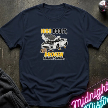 A navy blue graphic t-shirt laid flat on a dark textured surface. The shirt features a white car with its hood open, emitting smoke, with the text 'HIGH BOOST, BROKEN BANK ACCOUNT' in yellow and white.