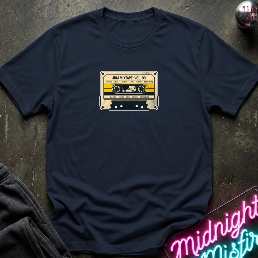 A navy blue crewneck t-shirt laid flat on a dark textured surface, featuring a retro cassette tape graphic on the chest with the text 'JDM MIXTAPE VOL.