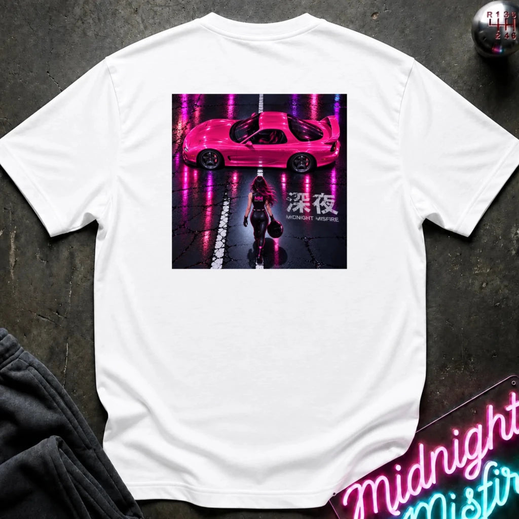A white short-sleeve t-shirt laid flat on a dark textured surface, featuring a large rectangular graphic print on the back. The graphic shows a pink sports car on a wet street with neon pink reflections and a person walking underneath, with the text 'Midnight' and Japanese characters.